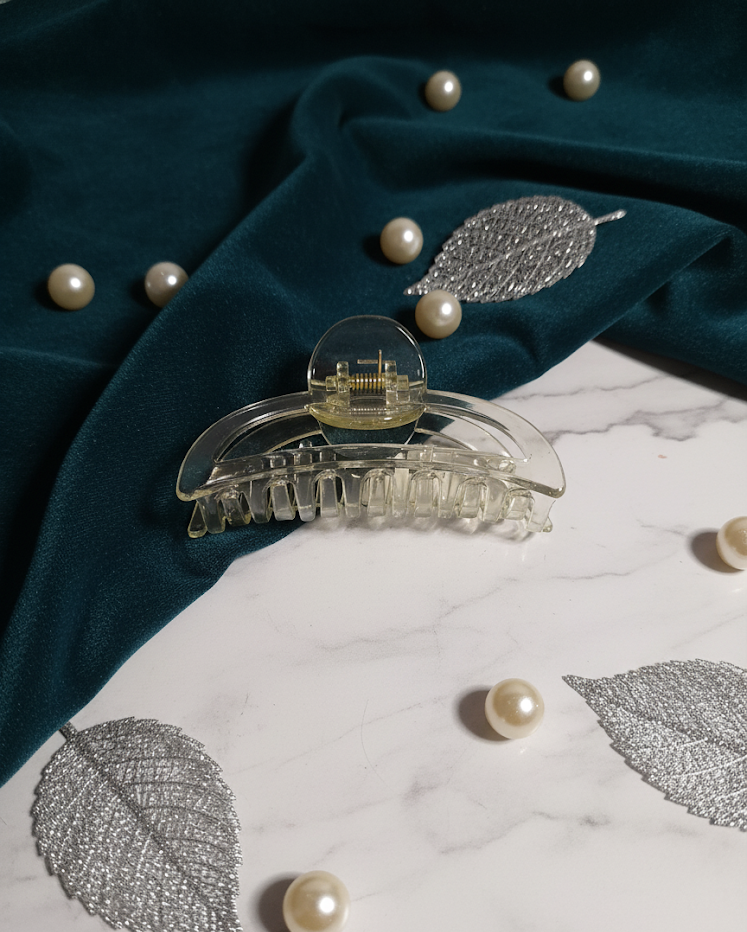 Clear hair clip on a dark fabric background with pearls and silver leaves.