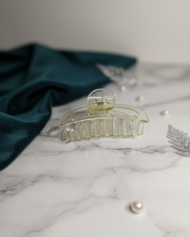 Clear hair clip on a marble surface with pearls and a green fabric
