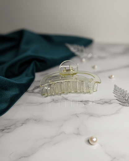 Clear hair clip on a marble surface with pearls and a green fabric